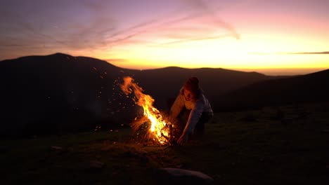 Camping-man-lights-a-bonfire-at-sunset-in-nature-with-mountain-view