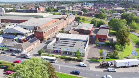 Drone-ascends-as-cars-and-buses-arrive-at-stop-light,-urban-industrial-setting-of-Rotherham-England