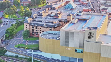 Drone-Desciende-A-Lo-Largo-Del-Exterior-De-La-Estructura-De-Estacionamiento-Del-Edificio-En-Un-Día-Soleado-Y-Vibrante