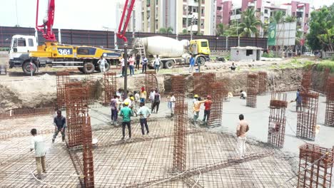 Aerial-drone-camera-moving-downwards,-construction-work-of-high-rise-building-is-in-progress-with-basement-being-built-and-concrete-and-cement-filling