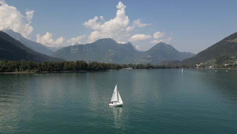 white-boat-with-sail-spread-anchored-parked-staying-on-one-spot-in-the-middle-of-lake-waves-are-moving-around-great-mountains-in-the-background-with-clouds-in-the-sky-amazing-view-of-nature-peaceful