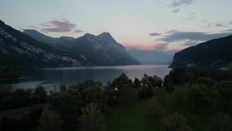 A-serene-pink-and-blue-sky,-dotted-with-light-clouds,-overlooks-the-mountainous-terrain-and-lush-vegetation-surrounding-Walensee-Lake