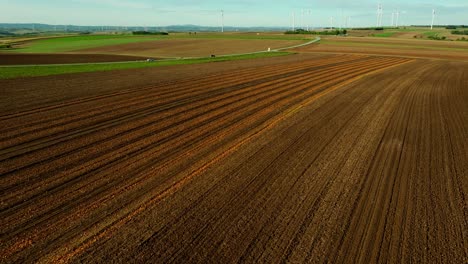 Scenic-Aerial-View-Of-A-Land-During-Harvest-Season-Near-Road-Overlooking-Wind-Turbines