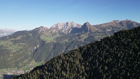 Toma-Aérea-De-Los-Alpes-Suizos-Y-Un-Lago-Situado-En-El-Valle-Cerca-Del-Bosque.