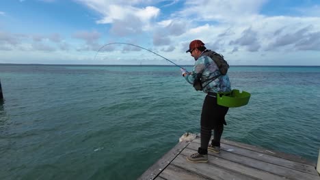 Hombre-Pesca-Deportiva-Macabí-Con-Caña-De-Pescar-En-Muelle-De-Madera,-Mar-Caribe-Los-Roques