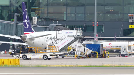 Airplane-with-a-purple-tail-logo-docked-at-an-airport-terminal-in-Gdansk-,-surrounded-by-ground-support-equipment-and-crew