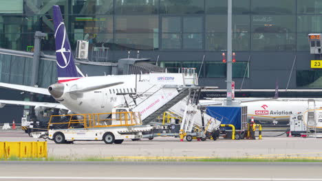 Flugzeug-Mit-Violettem-Hecklogo,-Das-An-Einem-Flughafenterminal-In-Danzig-Angedockt-Ist,-Umgeben-Von-Bodenunterstützungsgeräten-Und-Besatzung