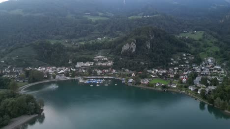 A-breathtaking-aerial-view-of-Walensee-and-Weesen-showcasing-the-navy-blue-waters,-residential-area,-and-the-Swiss-Alps-in-the-background