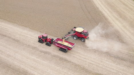 Combine-Harvester-Collecting-Grain-Crops-and-Transferring-Into-Grain-Cart-Attached-to-Tractor,-Aerial