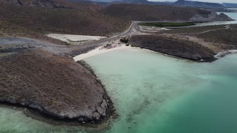 Aerial-shot-of-a-gorgeous-coastal-area-with-turquoise-calm-sea,-coastal-road-and-dry-landscape-in-Playa-El-Tecolote-near-La-paz-Baja-California-Sur-Mexico