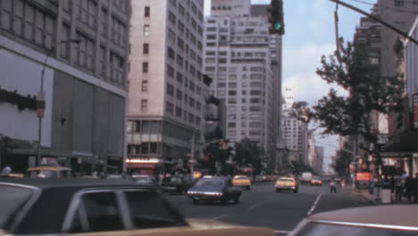 Una-Mujer-Se-Encuentra-En-Un-Paso-De-Peatones-En-Una-Avenida-Con-Autos-En-Nueva-York-En-Los-Años-1970