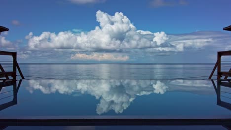 Cinematic-locked-off-shot-of-big-clouds-with-perfect-reflection-in-and-infinity-pool-at-a-luxury-tropical-beachside-resort