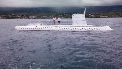 Gimbal-Weitwinkelaufnahme-Eines-Fahrenden-Bootes,-Das-Sich-Vom-U-Boot-Atlantis-Entfernt,-Während-Die-Besatzung-Vor-Der-Küste-Von-Kailua-Kona,-Hawaii,-Zum-Abschied-Winkt
