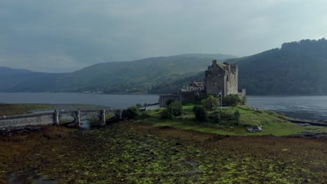 Eilean-Donan-Castle-in-the-highlands-of-Scotland,-UK-_-drone-shot-sunset-with-beautiful-lake-rising-up-side