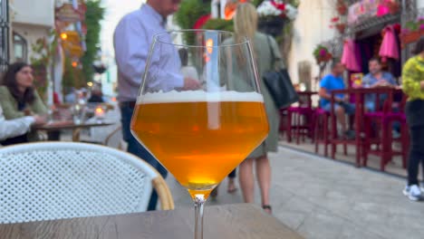 A-nice-cold-beer-in-a-busy-tourist-street-during-summer-in-Marbella-old-town-Spain,-blurry-people-sitting-and-having-food-outside-in-restaurants,-people-walking,-4K-shot
