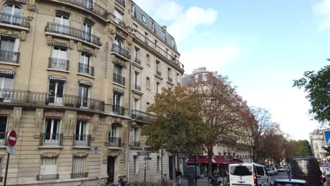 La-Gente-Camina-En-París-En-El-Parque-Buttes-Chaumont,-Anda-En-Bicicleta-Por-La-Calle,-Arquitectura-De-Apartamentos-Antiguos.