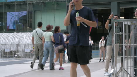 People-are-busy-walking-outside-of-Siam-Paragon-in-Bangkok-with-the-BTS-train-station-with-trains-leaving-and-stopping-for-passengers,-in-Thailand