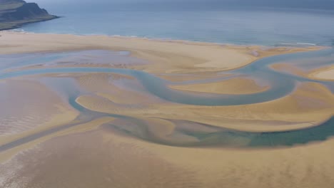 Aerial-panning-shot-of-red-sand-Raudasandur-beach-with-river-and-ocean-during-sunny-day---West-Fjord,-Iceland