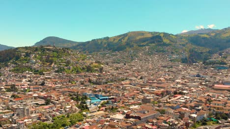 Vista-Aérea-De-La-Ciudad-De-Quito,-Capital-Del-Ecuador,-Edificios-Del-Centro-De-La-Ciudad-Bordeados-Por-Los-Cerros-De-Panecillo-E-Ichimbia