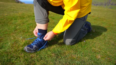 Close-up-shot-of-male-hands-tying-a-tall-blue-hiking-boot-on-the-grass
