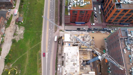 Aerial-top-down-shot-of-driving-cars-on-road-beside-construction-Site-with-crane-at-sunny-day