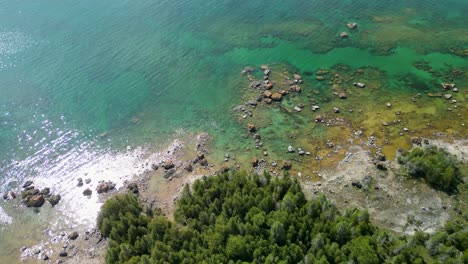 Aerial-view-pan-of-rocky-forested-shoreline-on-lake-huron,-Michigan