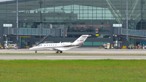 Privatjet-Auf-Einer-Landebahn-Mit-Einem-Verkehrsflugzeug-Und-Einem-Flughafenterminal-Im-Hintergrund