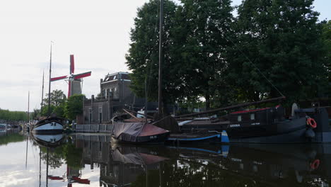 Molen-De-Roode-Leeuw-Mill-And-Old-Boats-In-Gouda,-Netherlands---wide