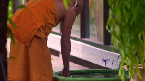 Buddhistischer-Mönch-In-Orangefarbenem-Gewand,-Zigarette-Rauchend,-Brunnenwasser-Reinigend