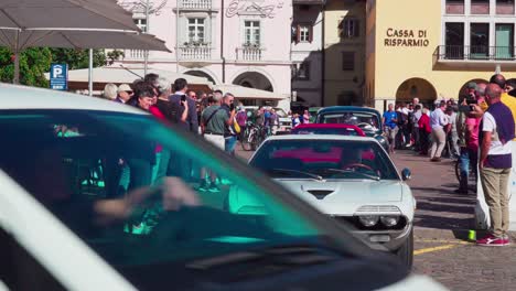 Oldtimer-Verlassen-Ihren-Treffpunkt-Am-Waltherplatz-In-Bozen,-Südtirol,-Während-Auf-Beiden-Seiten-Zuschauer-Stehen-Und-Den-Autos-Beim-Losfahren-Zusehen