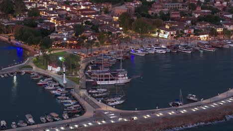 Aerial-view-circling-above-illuminated-Side-harbour-sailboats-and-Antik-Liman-coastal-Turkish-landmark-at-sunset