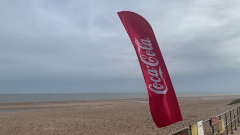 Una-Bandera-De-Coca-Cola-Suspiro-En-El-Viento-En-La-Playa-En-El-Paseo-Marítimo