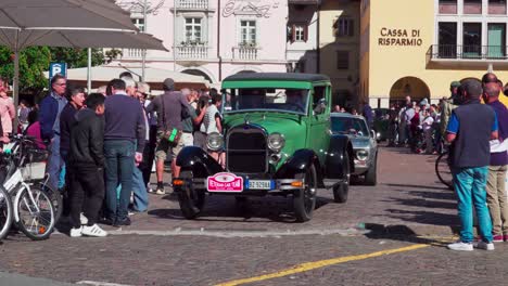 Oldtimer-Verlassen-Ihren-Treffpunkt-Am-Waltherplatz-In-Bozen,-Südtirol,-Während-Auf-Beiden-Seiten-Zuschauer-Stehen-Und-Den-Autos-Beim-Losfahren-Zusehen