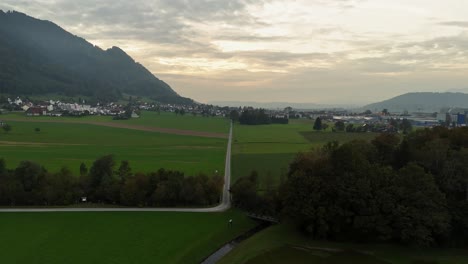Aerial-flyover-rural-road-between-grass-fields-in-Bilten-City-during-sunset-time,-Switzerland