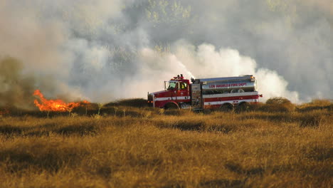 Firetruck-quelling-a-wildfire,-driving-and-hosing-water-on-forest-and-fields