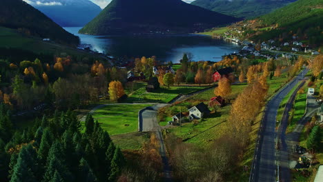Aerial-dolly-shot-over-a-beautiful-landscape-with-a-blue-lake-and-view-of-a-small-village-with-idyllic-buildings,-a-church-and-colorful-trees-in-the-middle-of-green-nature-during-a-trip-through-norway