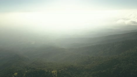 Pan-left-and-fly-over-mountain-range-during-sunrise-with-haze-and-white-light