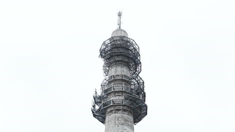 Aerial-low-angle-ascending-shot-of-a-bleak-industrial-concrete-television-and-radio-link-tower-in-Pasila,-Helsinki,-Finland-on-a-bright-and-foggy-day