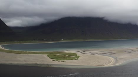 Vista-Aérea-Del-Fiordo-Onundarfjordur-Con-Isla-Arenosa-Y-Montañas-Verdes-Cubiertas-Por-Densas-Nubes