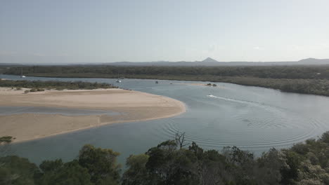Flyover-coastal-jungle-reveals-boaters-on-shallow-Noosa-River,-QLD-AUS