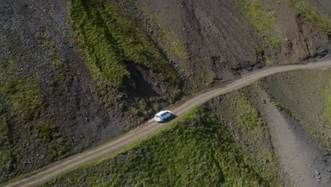 Aerial-tracking-shot-of-driving-car-on-mountain-road-during-sunny-day---Svalvogavegur,-Europe