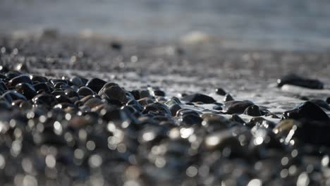 Extreme-close-up-of-waves-washing-up-on-a-stony-beach-with-dark-and-brown-tones-and-highlights-from-the-shine-on-the-rocks
