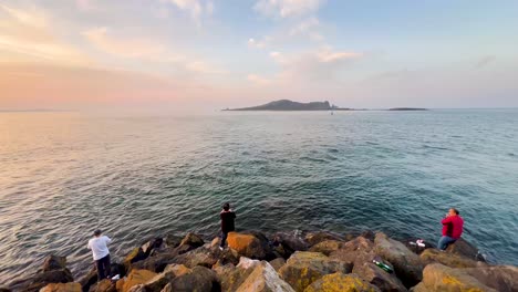 Pesca-En-El-Muelle-De-Howth:-Serena-Puesta-De-Sol-Con-Pescadores,-Costa-Rocosa-Y-Aguas-Tranquilas-Junto-Al-Mar