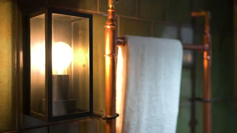 Close-up-of-old-fashioned-artisian-bathroom-lamp-on-wall-next-to-rustic-towel-rail-in-countryside-cabin-interiors-features