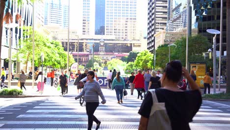 Statische-Aufnahme,-Die-Büroangestellte-Und-Die-Allgemeine-Öffentlichkeit-Beim-Überqueren-Der-Queen-Street-Am-Post-Office-Square-Mit-Dem-Hauptbahnhof-Im-Hintergrund-Während-Der-Hauptverkehrszeiten-Im-Zentralen-Geschäftsviertel-Von-Brisbane-Zeigt