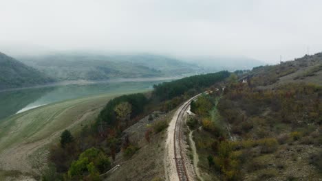 Aerial-view-of-train-tracks-on-a-mountain-side-surrounded-by-autumn-trees-and-a-foggy-sky-in-the-background