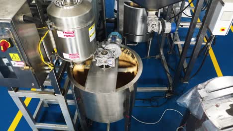 Aerial-side-view,-peanut-butter-being-ground-into-peanut-butter-in-a-peanut-butter-manufacturing-plant