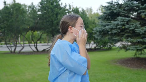 Woman-putting-on-her-facemask-and-secures-its-tightness-on-her-face-while-wearing-lab-coat,-static