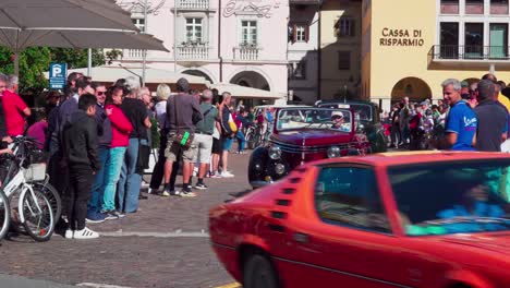 Oldtimer-Verlassen-Ihren-Treffpunkt-Am-Waltherplatz-In-Bozen,-Südtirol,-Während-Auf-Beiden-Seiten-Zuschauer-Stehen-Und-Den-Autos-Beim-Losfahren-Zusehen