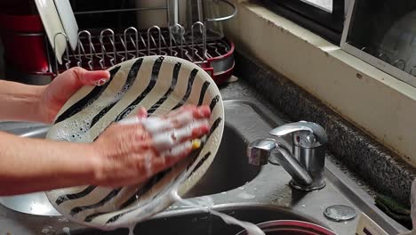 Man-washes-the-dishes-with-the-cleaning-sponge-while-he-is-watching-videos-on-a-tablet